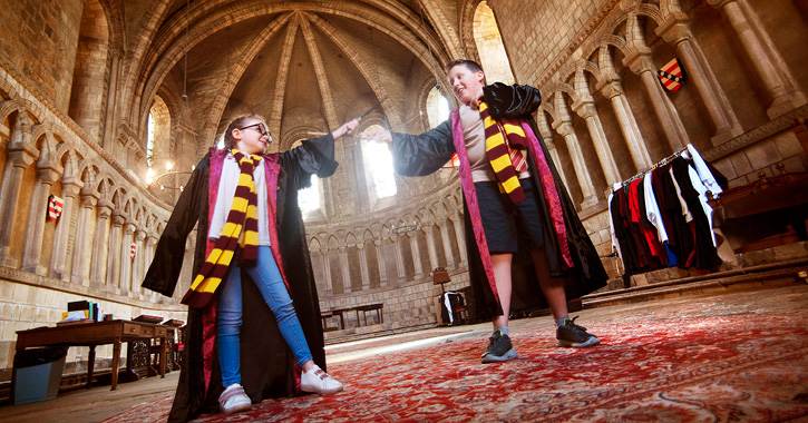 Two kids dressed in wizard robes playing with wands inside the Chapter House, Durham Cathedral